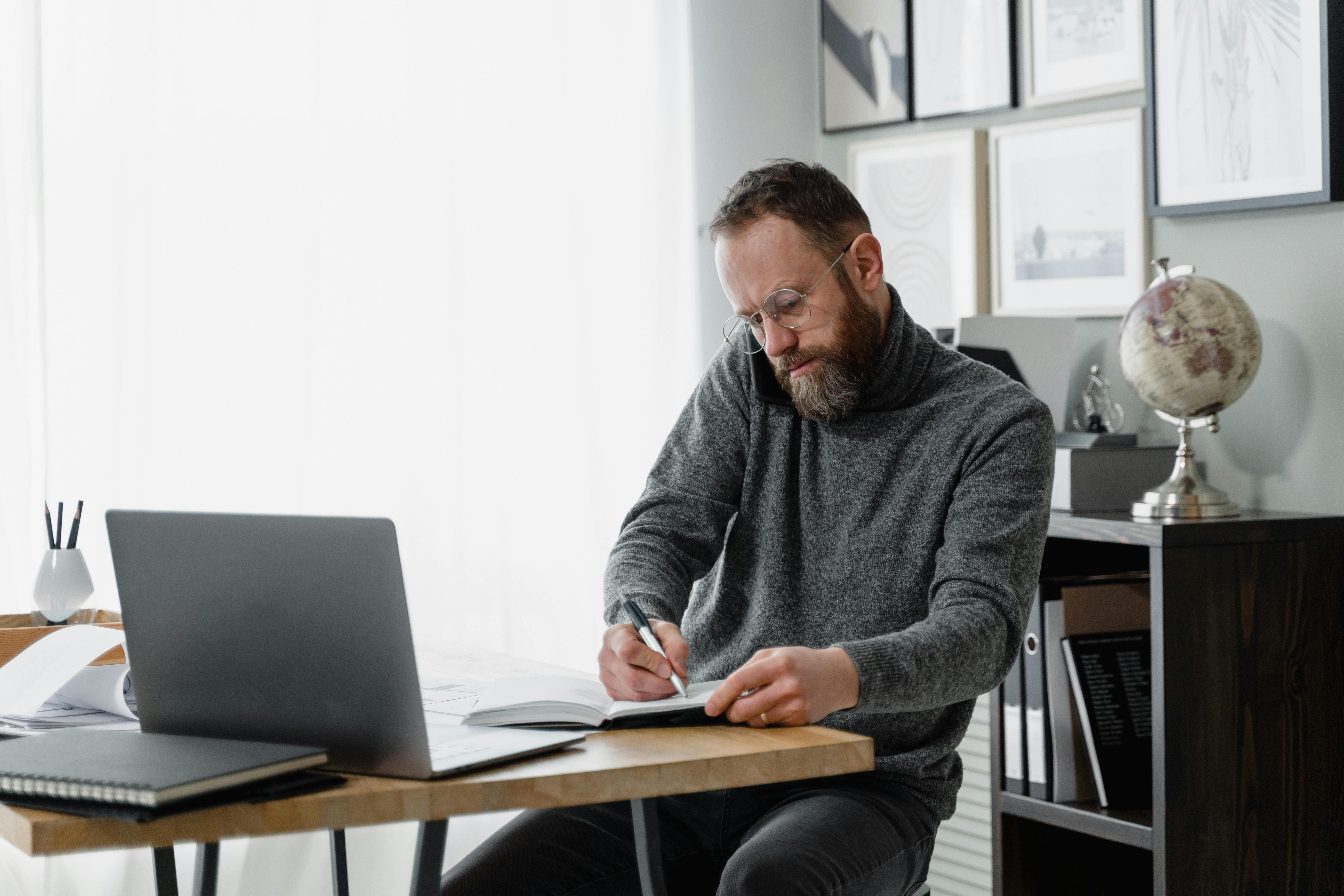 Man concentrating on work at home office desk with laptop and documents.