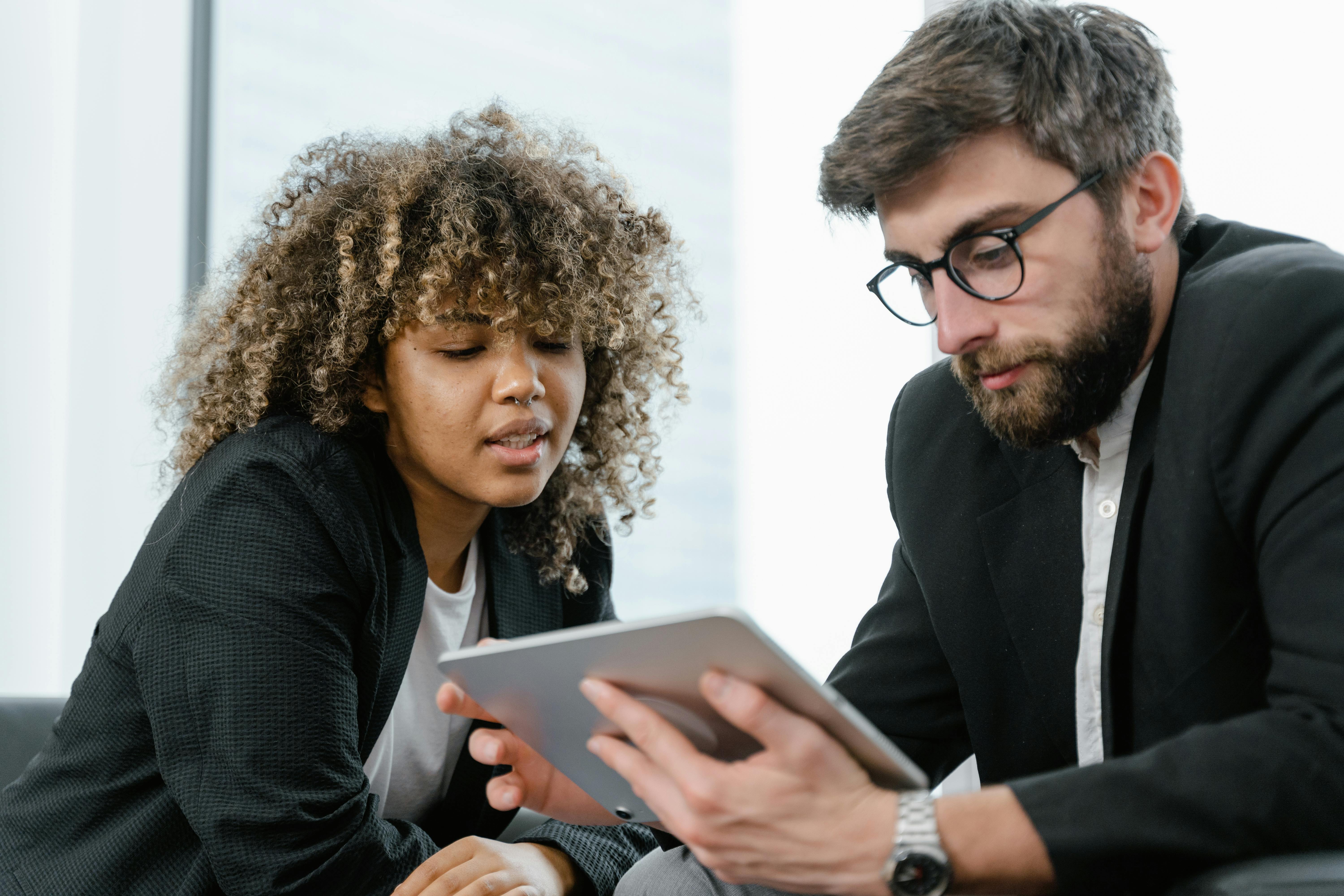 Two business professionals reviewing data on a tablet, fostering collaboration and teamwork in a modern office setting.